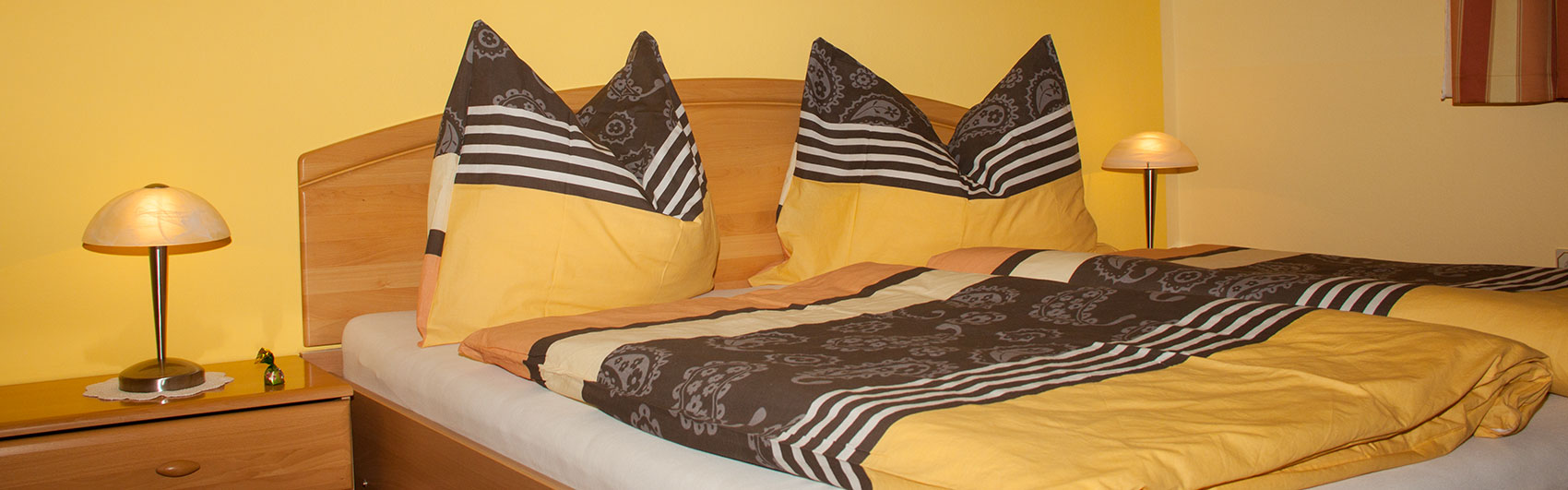 Blick auf das frisch bezogene Doppelbett mit Nachtkästchen und Lampen.